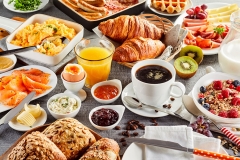 Huge healthy breakfast spread on a table with coffee, orange juice, fruit, muesli, smoked salmon, egg, croissants, meat and cheese