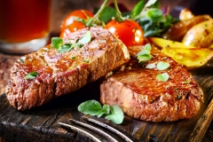 Succulent thick juicy portions of grilled fillet steak served with tomatoes and roast vegetables on an old wooden board